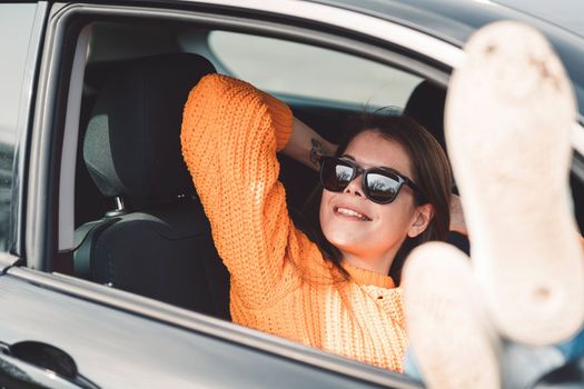 Beautiful young happy smiling caucasian woman driving in her car, wearing sunglasses and an orange sweater. High quality photo