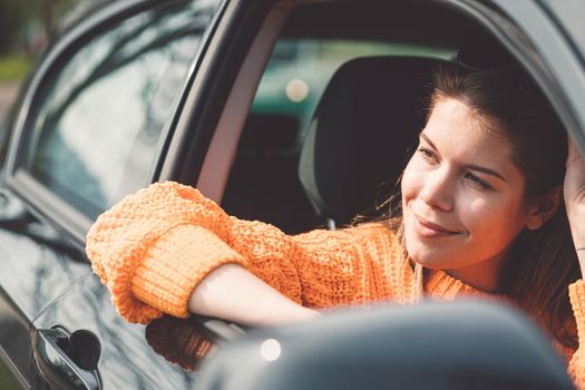 Beautiful young happy smiling caucasian woman driving in her car, wearing sunglasses and an orange sweater. High quality photo