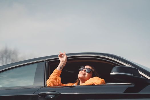 Beautiful young happy smiling caucasian woman driving in her car, wearing sunglasses and an orange sweater. High quality photo