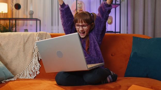 Surprised toddler girl child kid use laptop computer, receive good news message, shocked by sudden victory, celebrate win, lottery jackpot, purchases online shopping at home. Lifestyle technologies