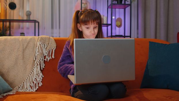 Portrait of caucasian toddler girl use laptop typing browsing working, loses becoming surprised sudden lottery results, bad news, fortune loss, fail. Teen child kid at home in play room on couch