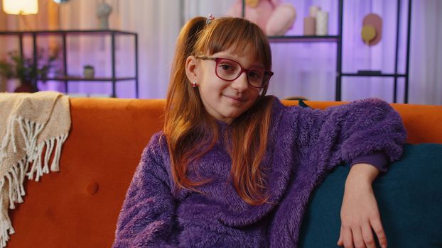 Happy calm teen toddler girl child kid 7 years old smiling friendly, glad expression looking at camera dreaming resting, relaxation feel satisfied concept good news on couch. Teen children at home