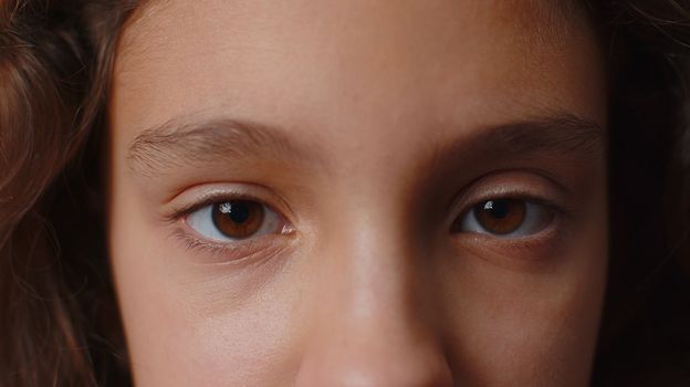 Extreme close-up macro portrait of smiling girl face. Teen beautiful kid's eyes, looking at camera. Brown eyes of brunette female child model. Young positive cute children opening wide her closed eyes