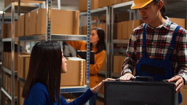 Male worker helping business owner in warehouse, checking stacks of products and retail store supplies. Asian people planning transportation with laptop using stock distribution, online shipment.