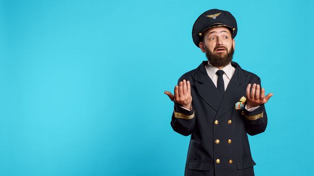 Confused plane aviator acting shocked and surprised, feelig uncertain and being in shock on camera. Professional airline captain having surprised reaction over blue background, commercial pilot.