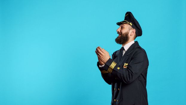 Male aviator applauding and cheering on camera, saying congratulations and clapping hands in studio. Airline pilot in flying uniform with cheerful emotions doing standing ovation sign.