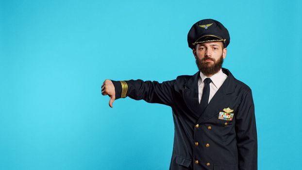 Professional aviator showing thumbs down sign, expressing dislike and bad negative gesture. Airline pilot in uniform doing disapproval and failure symbol, commercial flights occupation.