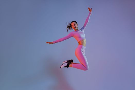 Athletic active woman jumping on studio background with colored filter. Dynamic movement