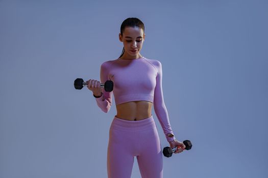 Woman doing exercises with dumbbells on studio background . Sport and healthy lifestyle