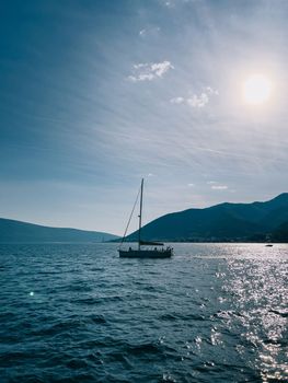 Sailing yacht sails on the sea under bright sunbeams against the backdrop of mountains. High quality photo