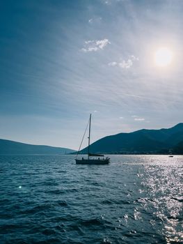 Sailing yacht sails on the sea under bright sunbeams against the backdrop of mountains. High quality photo