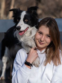 Caucasian woman hugging her dog Border Collie while sitting on a bench in autumn park