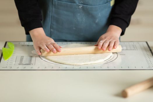 Rolling out the dough with a wooden rolling pin on a silicone baking mat. View of hands and workspace. copy space.