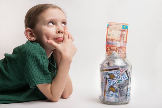 Happy girl with a large transparent jar with Kazakhstani tenge money. the child thought about new toys and gadgets.