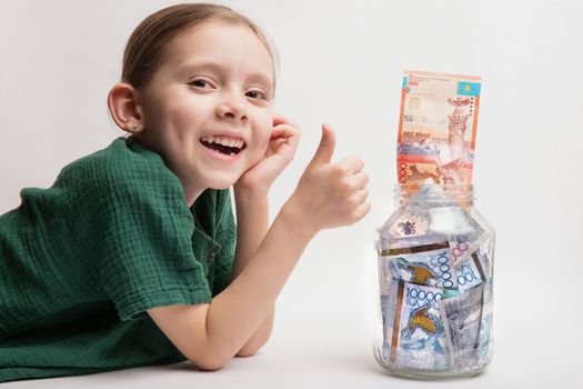 Kid with a large transparent jar with Kazakhstani tenge money. Bank account for a child.