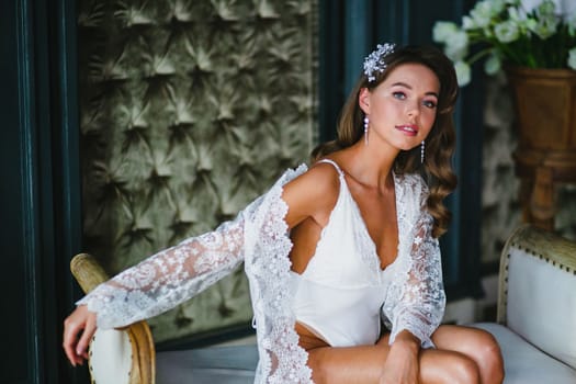 Bride's fees in the hotel room - close-up portrait of seductive young bride in white negligee and lingerie preparing to wedding ceremony