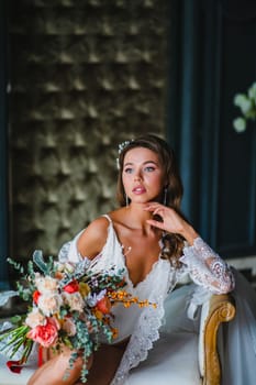 Close-up portrait of young bride in white negligee and lingerie posing with gorgeous bridal bouquet in the hotel room