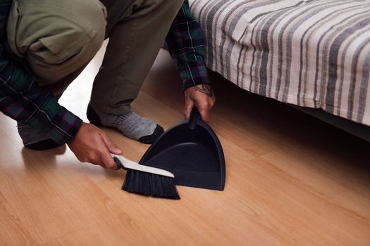 close up of the hands of a man cleaning the floor with a brush and dustpan, home cleaning concept, copy space for text