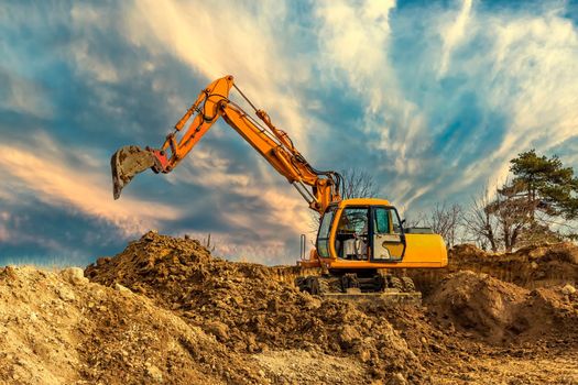 Crawler excavator during earthmoving works on construction site at sunset