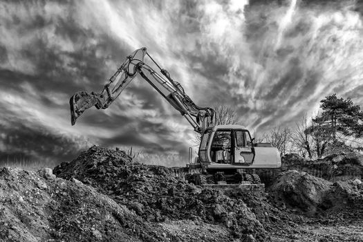 Crawler excavator during earthmoving works on construction site in black and white