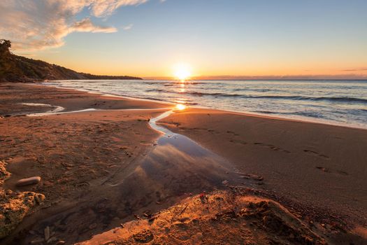 Sea sunrise with a small brook flowing into the sea 
