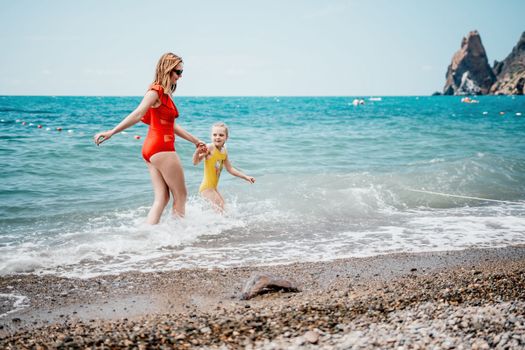 Happy loving family mother and daughter having fun together on the beach. Mum playing with her kid in holiday vacation next to the ocean - Family lifestyle and love concept.