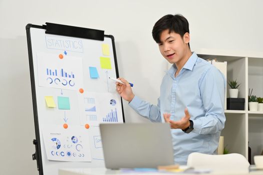 Confident businessman explaining business data on whiteboard during online conference via laptop computer.