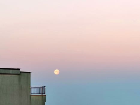 the moon on the pink blue morning sky next to the terrace of the house.