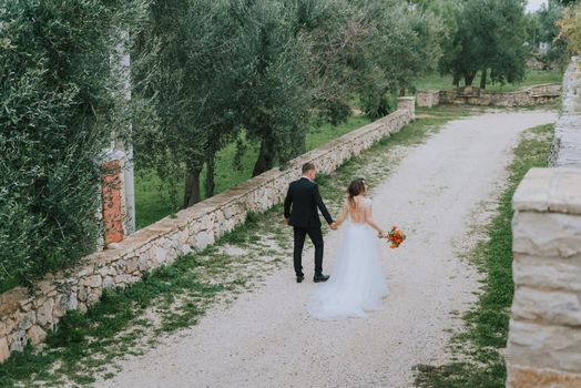 Happy stylish smiling couple walking in Tuscany, Italy on their wedding day. The bride and groom walk down the street by the hands. A stylish young couple walks. Husband and wife communicate nicely. Lovers run through the streets of the city.