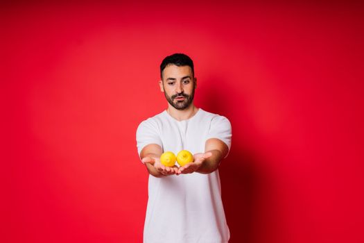 Portrait of young bearded man holding lemons in both hands on an isolated red background