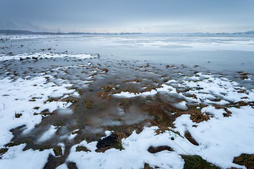 Melting snow with water on the meadow and cloudy sky, january day in Czulczyce, Poland.