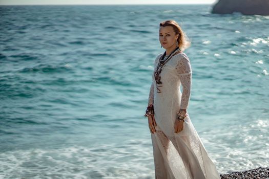 Woman beach sea white dress. The middle-aged looks good with blonde hair, boho style in a white long dress with beach decorations on the neck and arms