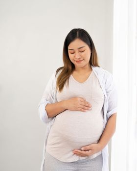 pregnant woman standing near window at home.