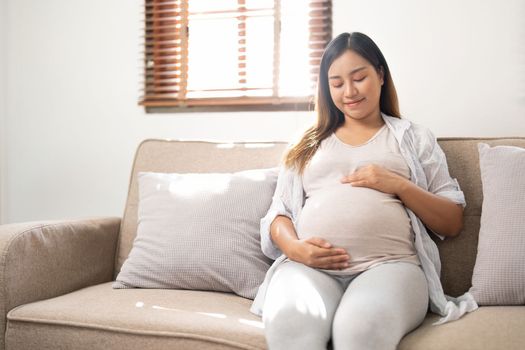 pregnancy, rest, people and expectation concept - close up of happy smiling pregnant woman in and touching her belly at home.