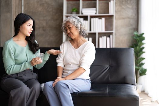 Unhappy Asian mother refuse taking medicines from her daughter hand.