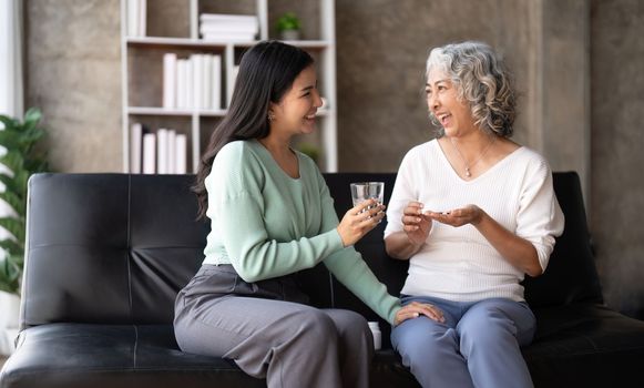 Asian daughter giving pills to mother helping her mom taking medicine with glass of water.