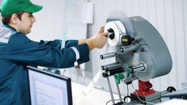 The worker changes paper roll with marking stickers on a machine with automated marking. High quality photo