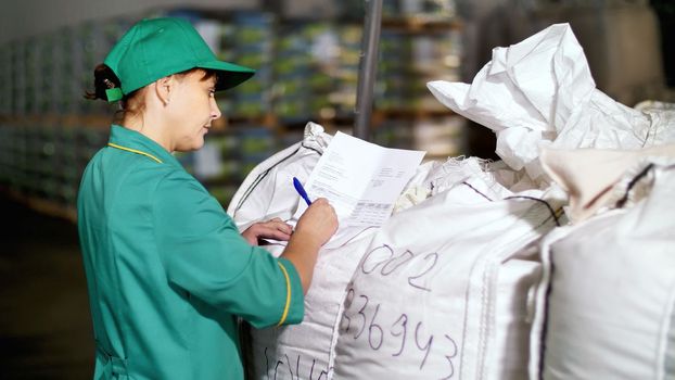 portrait of woman, employee of agricultural enterprise, fills out paper sheets on big bags in the warehouse. storage of agricultural products. High quality photo