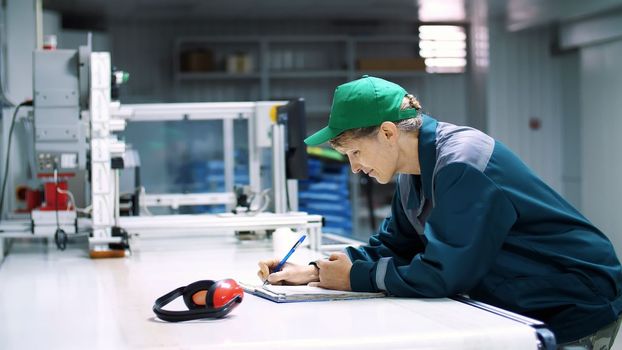 elderly woman, employee, worker at an enterprise, factory, fills up a service journal, record book, working industrial background. High quality photo
