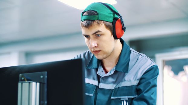 portrait of an employee of an enterprise, factory. a worker in red headphones from noise, looks at a computer monitor, adjusts, controls work of machines, automated production. High quality photo