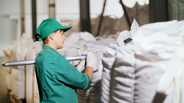 woman, employee of agricultural enterprise, takes samples of corn grain from big bags in warehouse for analysis in lab. High quality photo