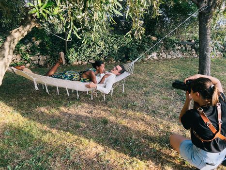 Girl photographer photographs a laughing woman lying on a man in a hammock. High quality photo