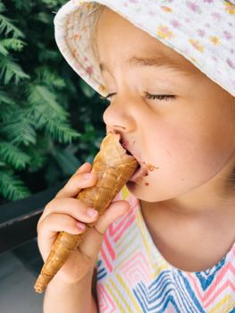 Little girl nibbles on an ice cream waffle cone with her eyes closed. High quality photo