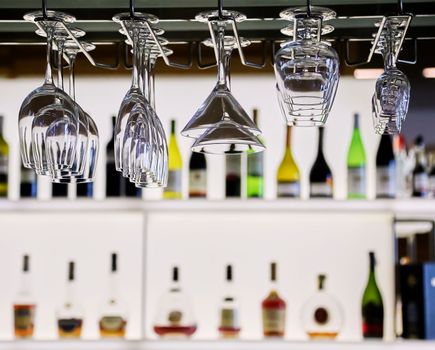 Glasses in the bar, restaurant interior. Clean glasses hang against the background of wine bottles.