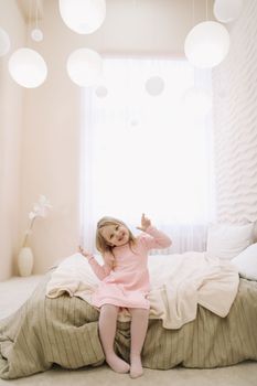 Morning of little girl in a comfortable bedroom. Happy child girl having fun and plays in bed.