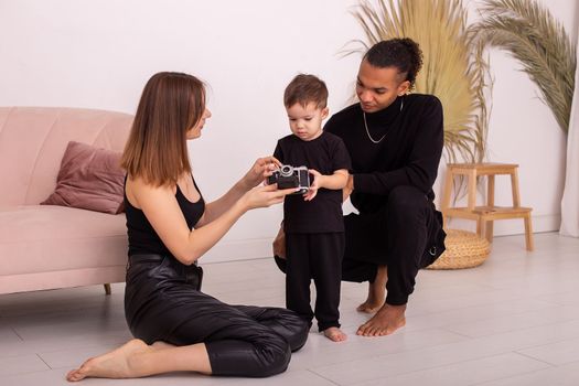 Stylish multiracial young family in black clothes, in the light living room, playing with an old camera