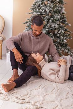 A happy girl, lies on the lap of a stylish guy near the Christmas tree in the room.Vertical