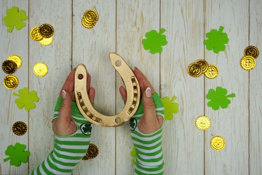 Women's hands hold a golden horseshoe on St. Patrick's Day. St. Patrick's Day celebration. The golden horseshoe. Coins and clover leaves on a wooden background.