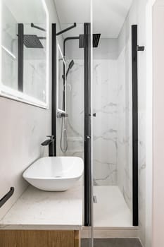 Bathroom with modern designer renovation and fittings. Vanity sink with black faucet. Walls of white granite tiles and square mirror with built-in light