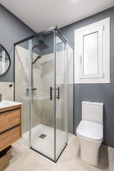 Bathroom in a modern style with high-quality design and expensive fittings. Gray walls are in harmony with black metal decor. Daylight enters through window in wall brightly illuminating room